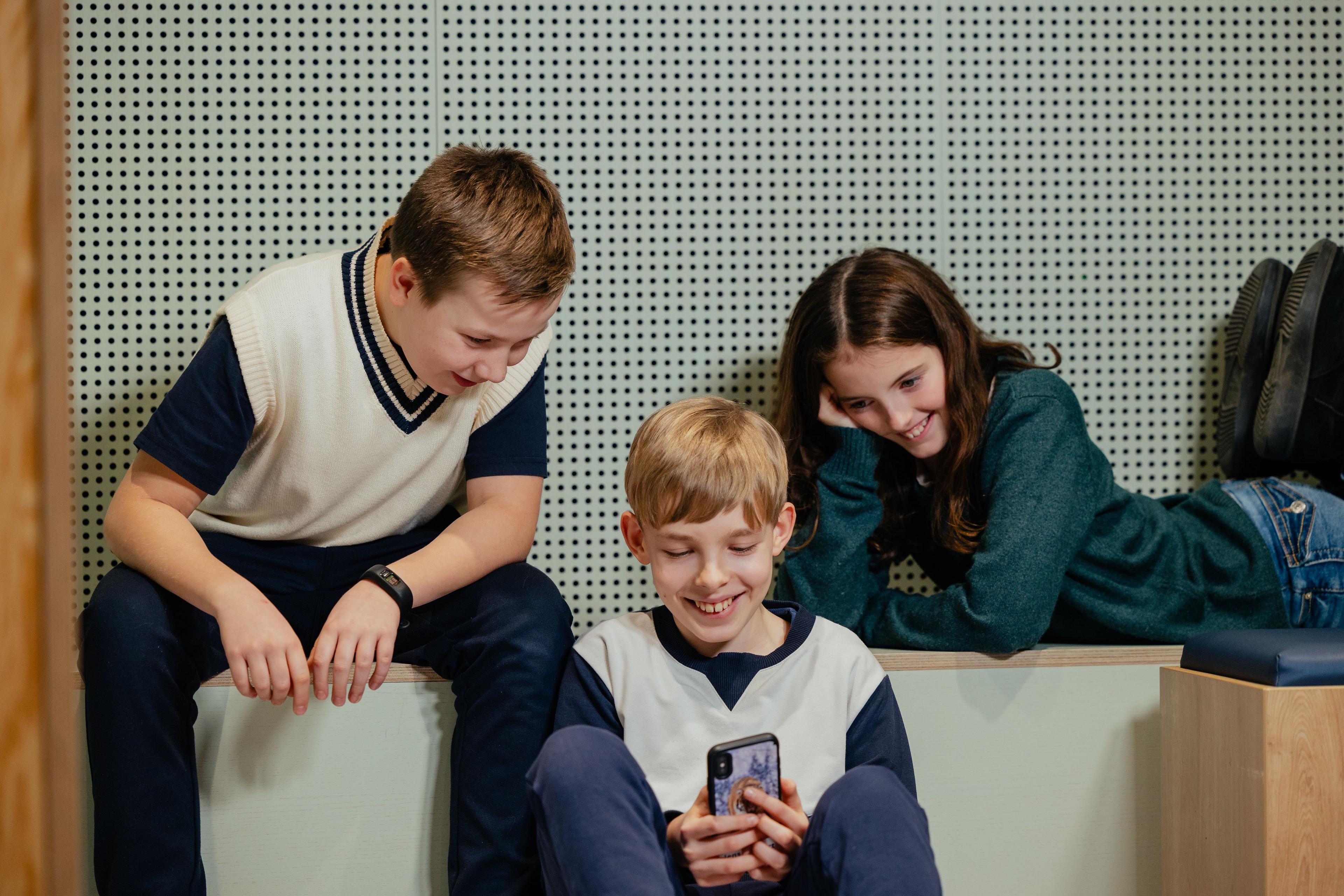 Tre børn hygger sig og har det sjovt sammen med en smartphone