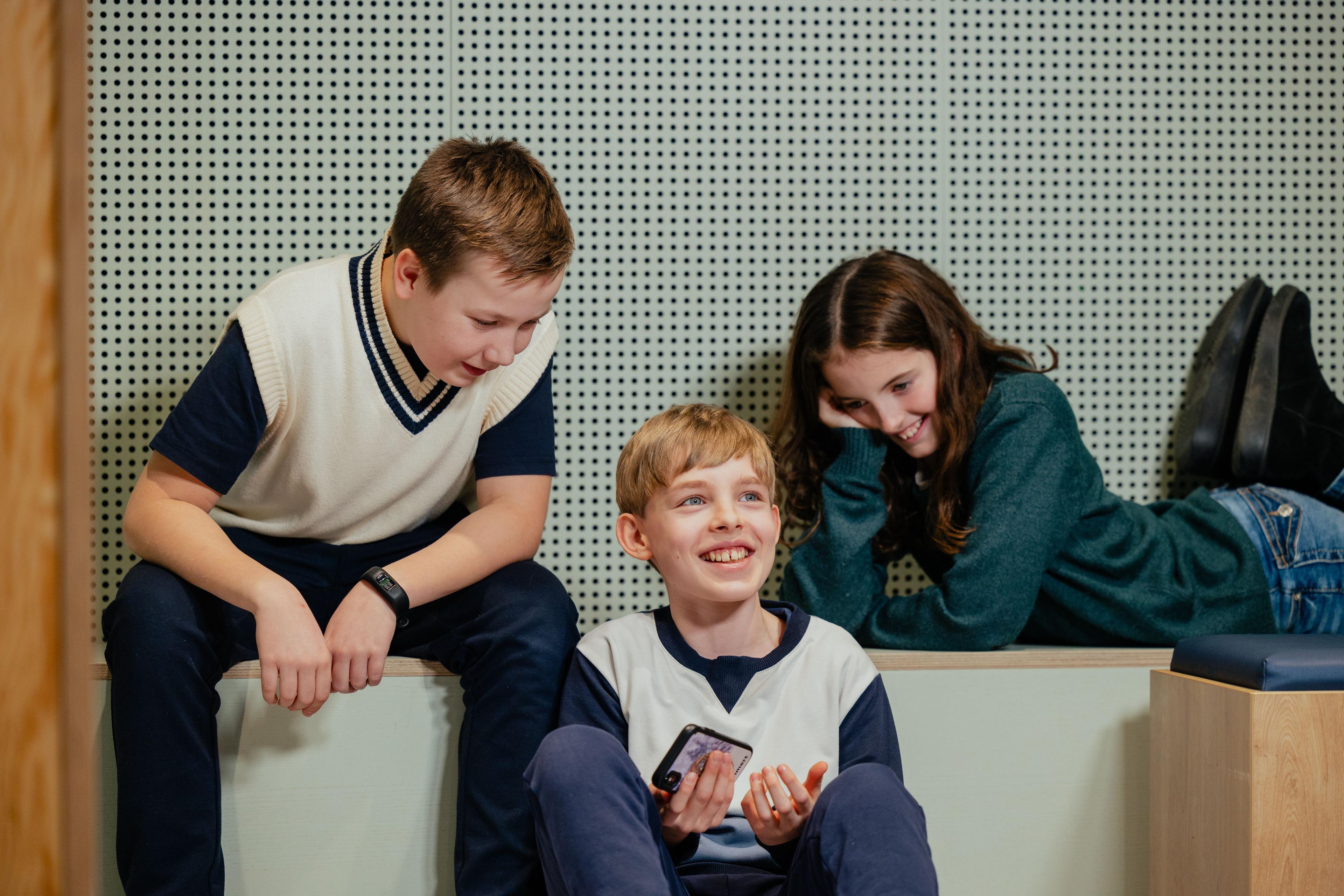 Tre børn hygger sig og har det sjovt sammen med en smartphone