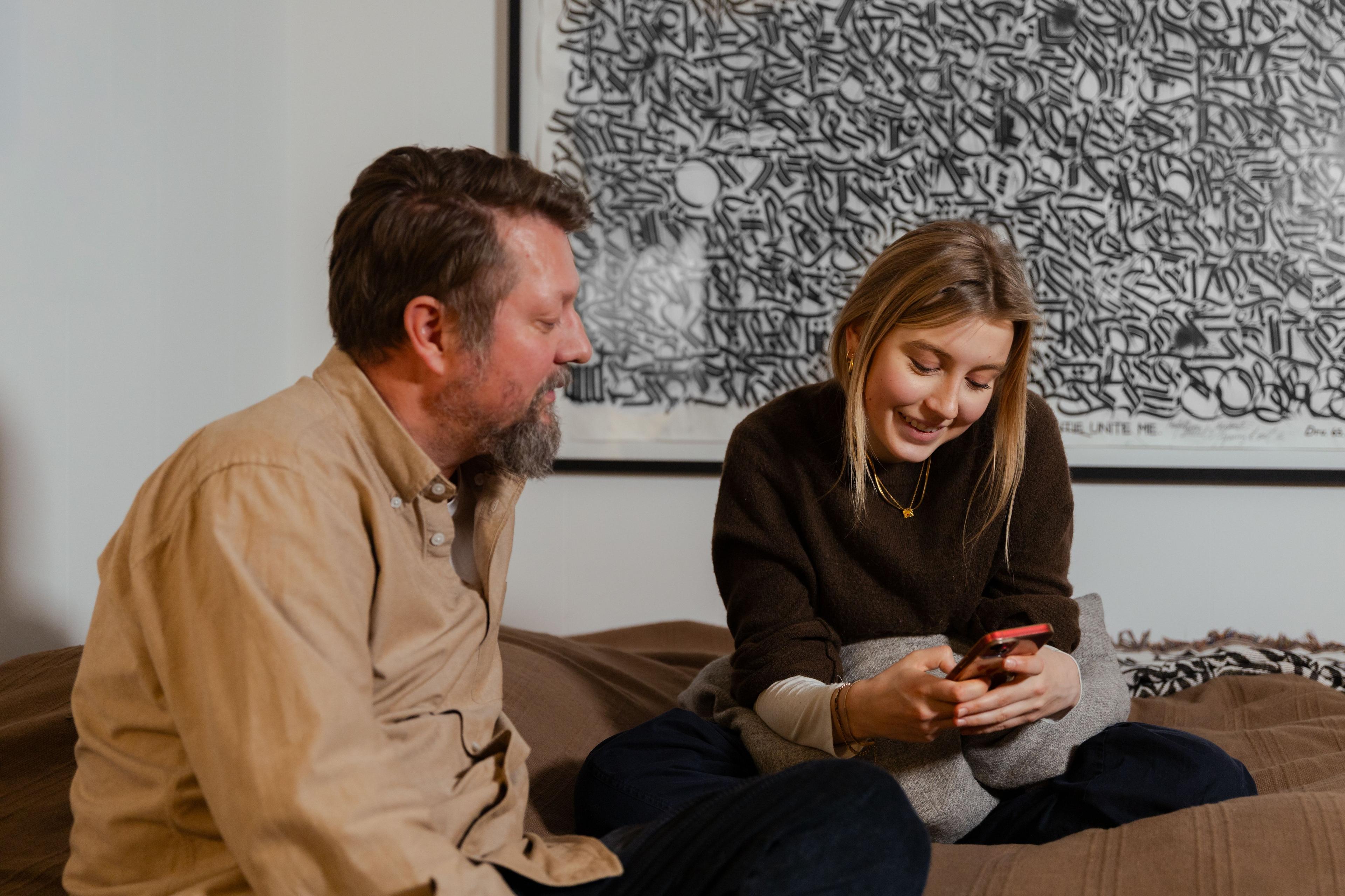 voksen og teenager sidder i sofa, kigger på smartphone