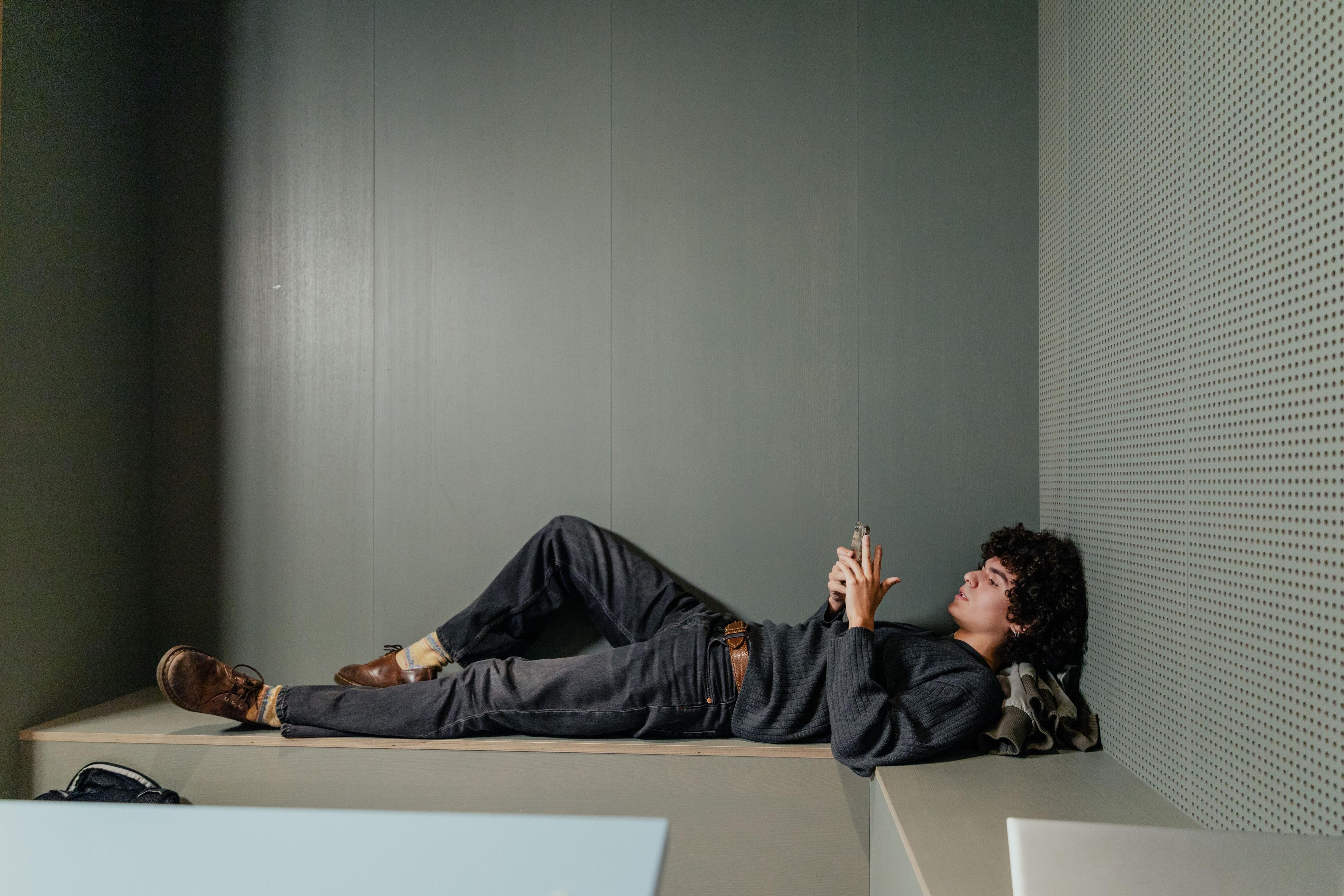 Teenagedreng liggende på bænk med sin mobil